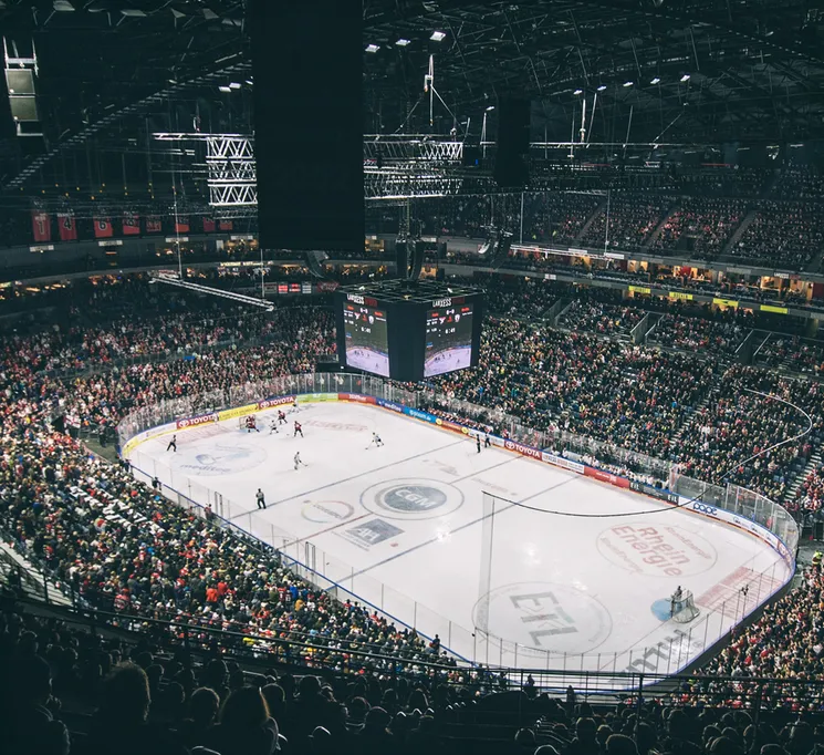 A wide view of a packed ice hockey arena with players on the ice and a large scoreboard.