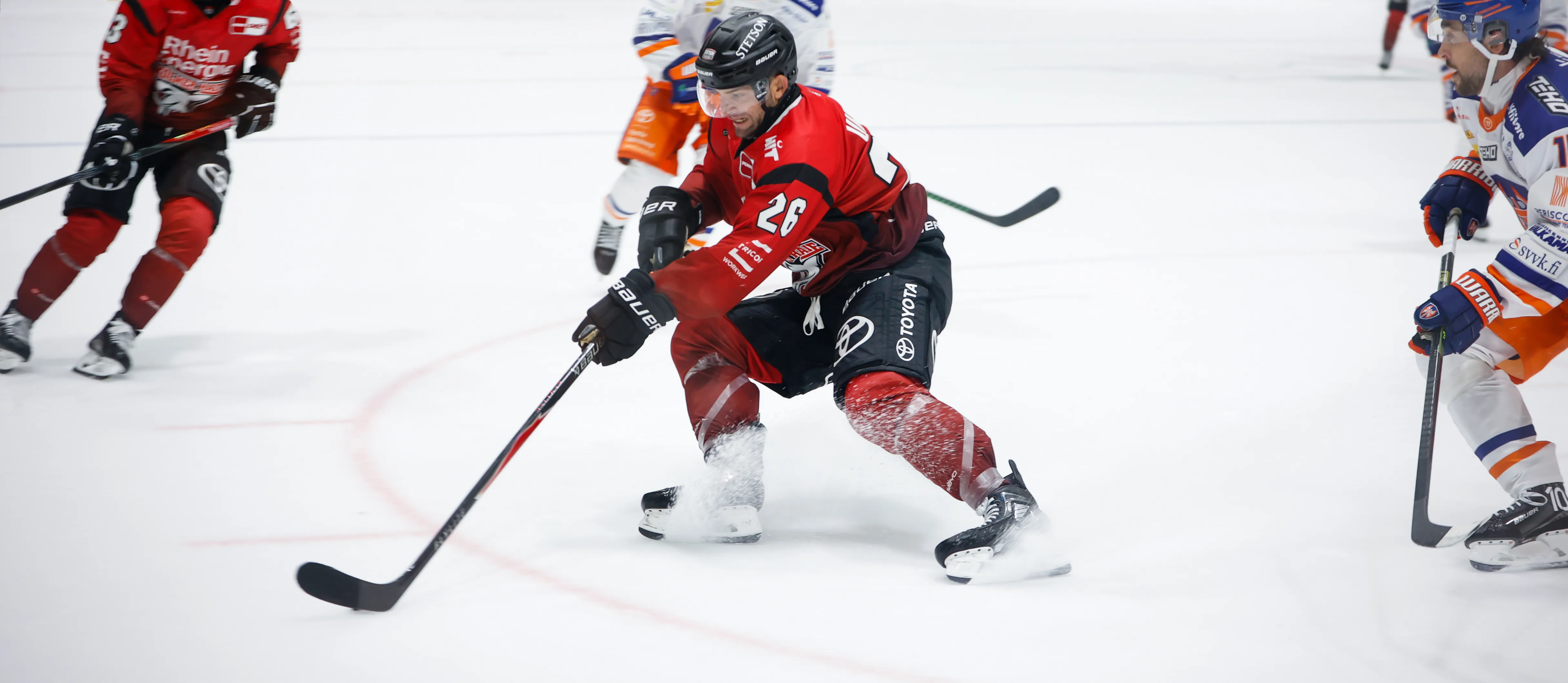 An ice hockey player in red sportswear is dribbling the puck on the ice.
