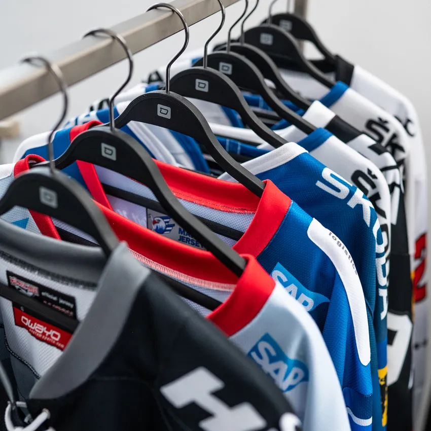 Several colorful ice hockey jerseys are hanging on a clothes rack.