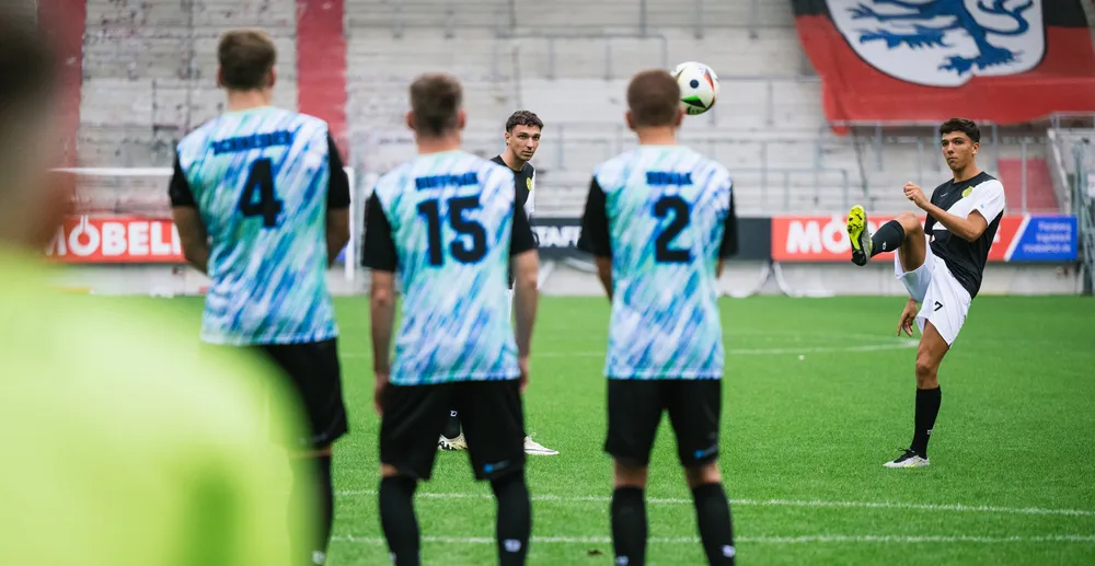 A soccer player is taking a shot while other players in colorful jerseys watch.