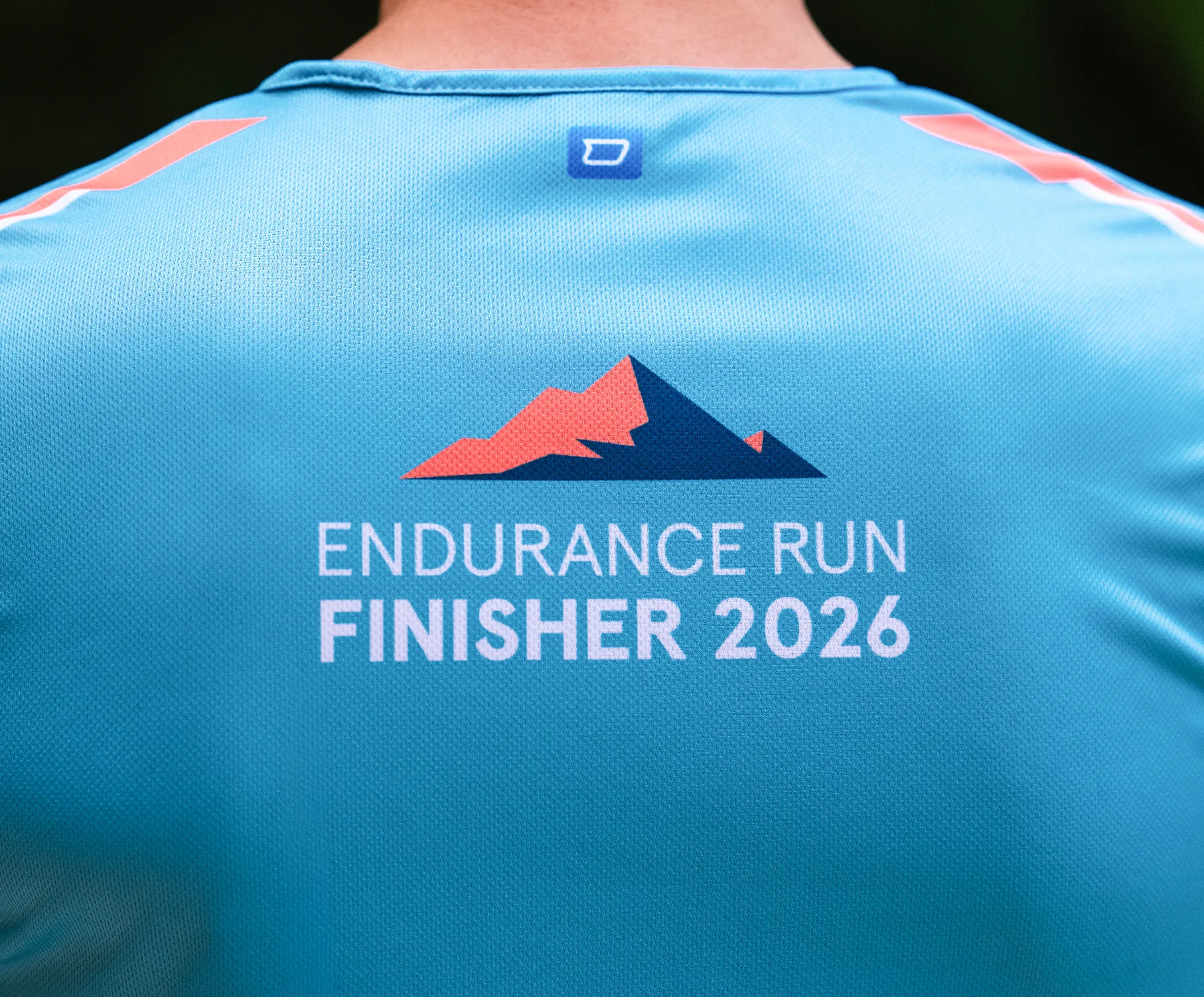 A blue sports shirt featuring the print 'ENDURANCE RUN FINISHER 2026' and a stylized mountain design on the back.