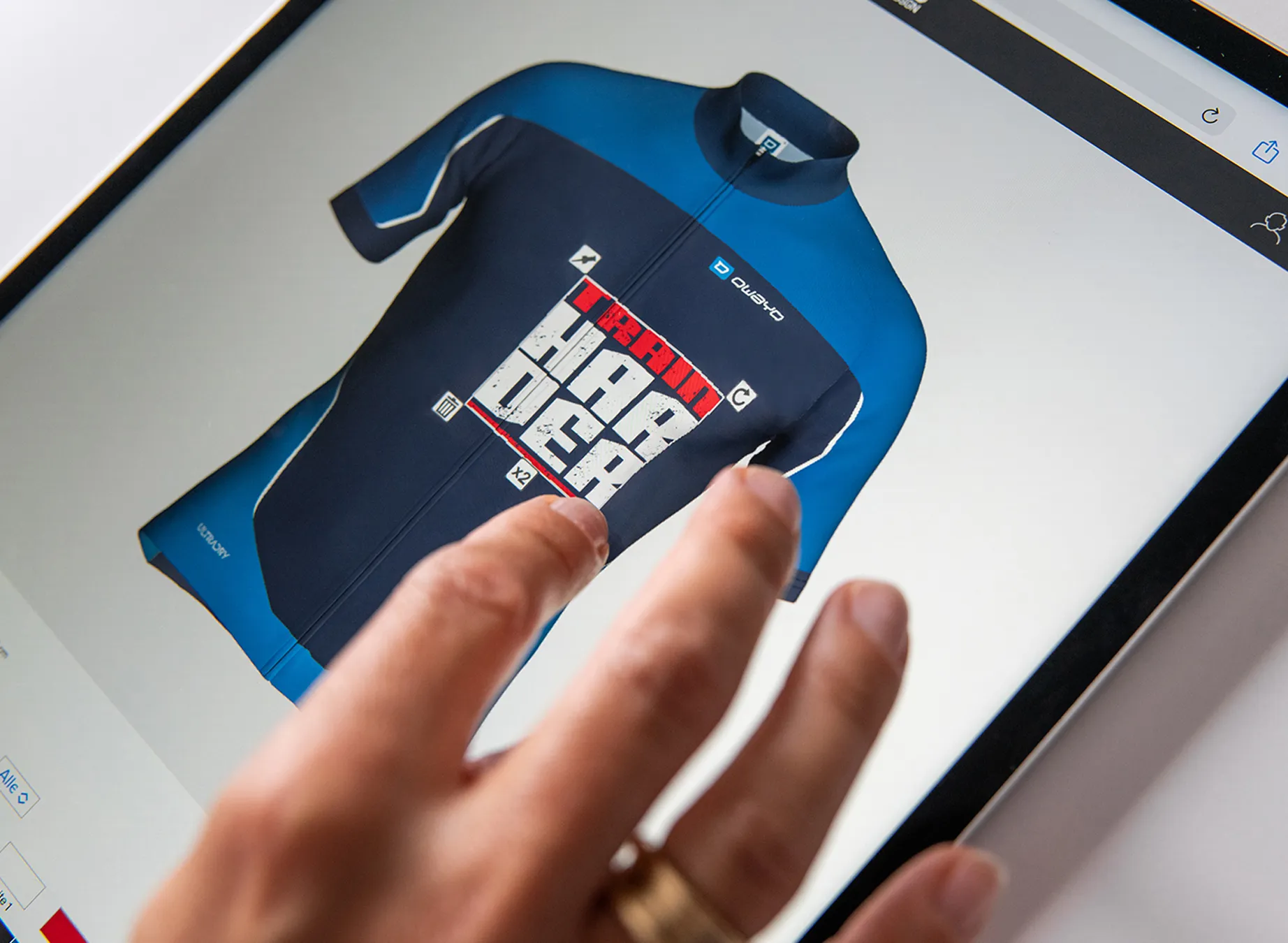 A hand points at a digital design of a blue sports jersey featuring the text 'train harder'.