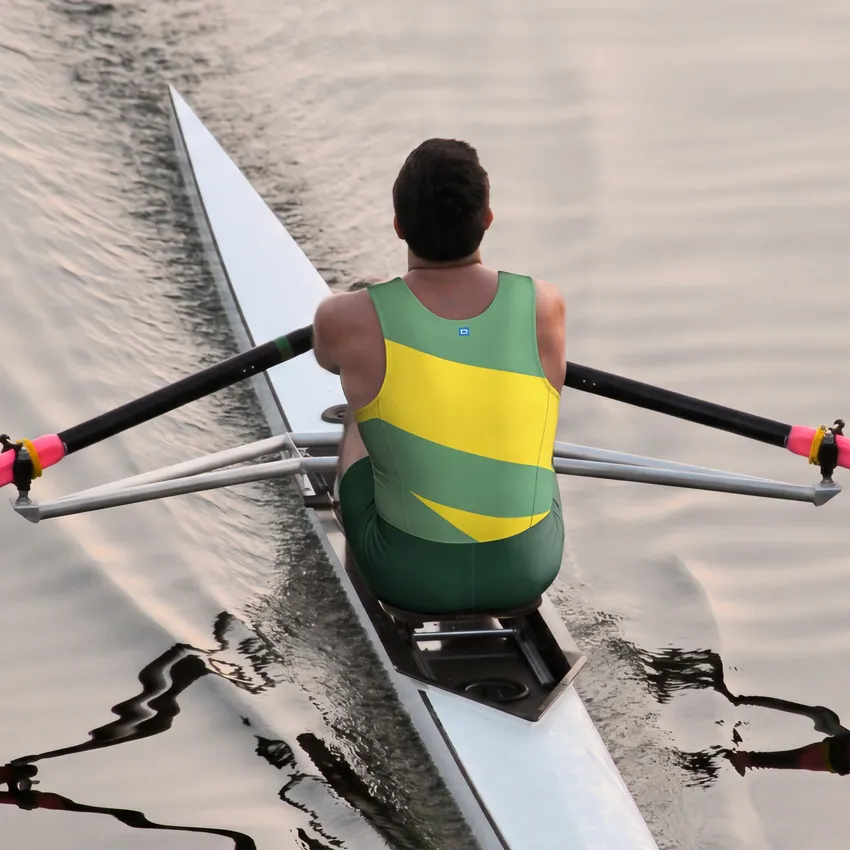 A rower in a green and yellow one-piece suit is rowing on calm water.