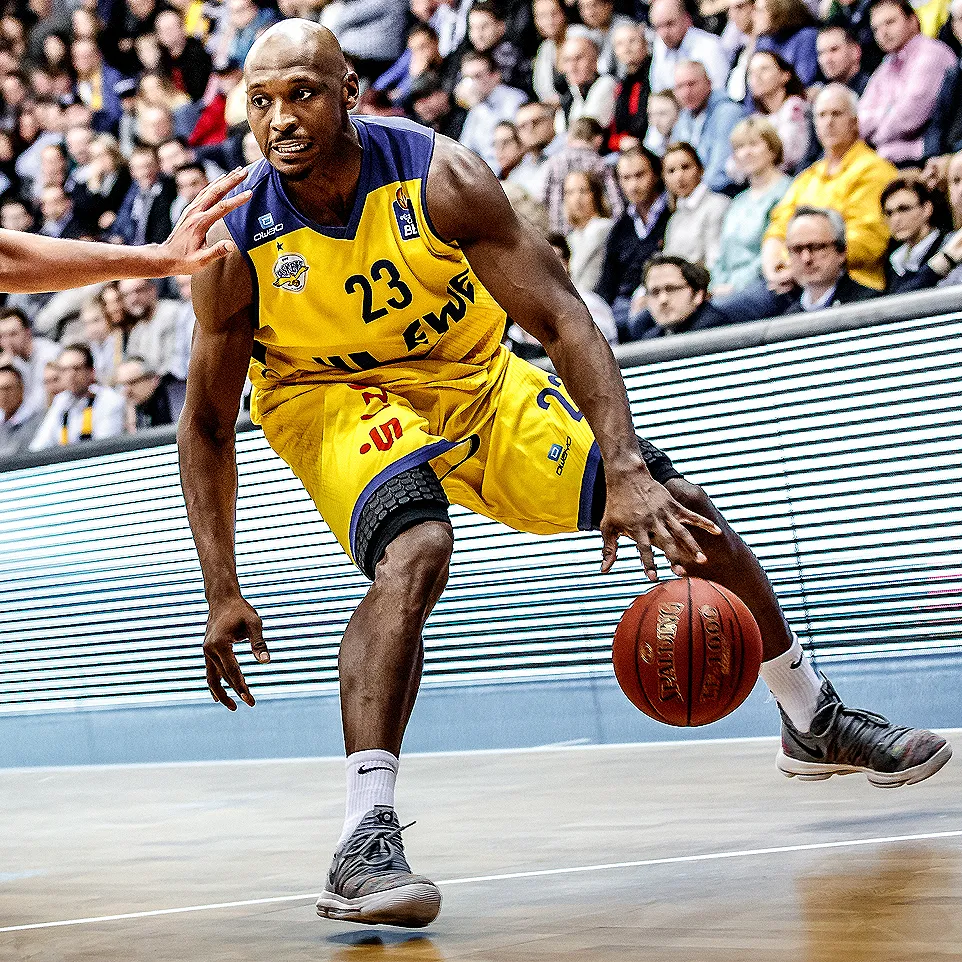 A basketball player in a yellow jersey with the number 23 dribbles a ball on a basketball court in front of a crowd.